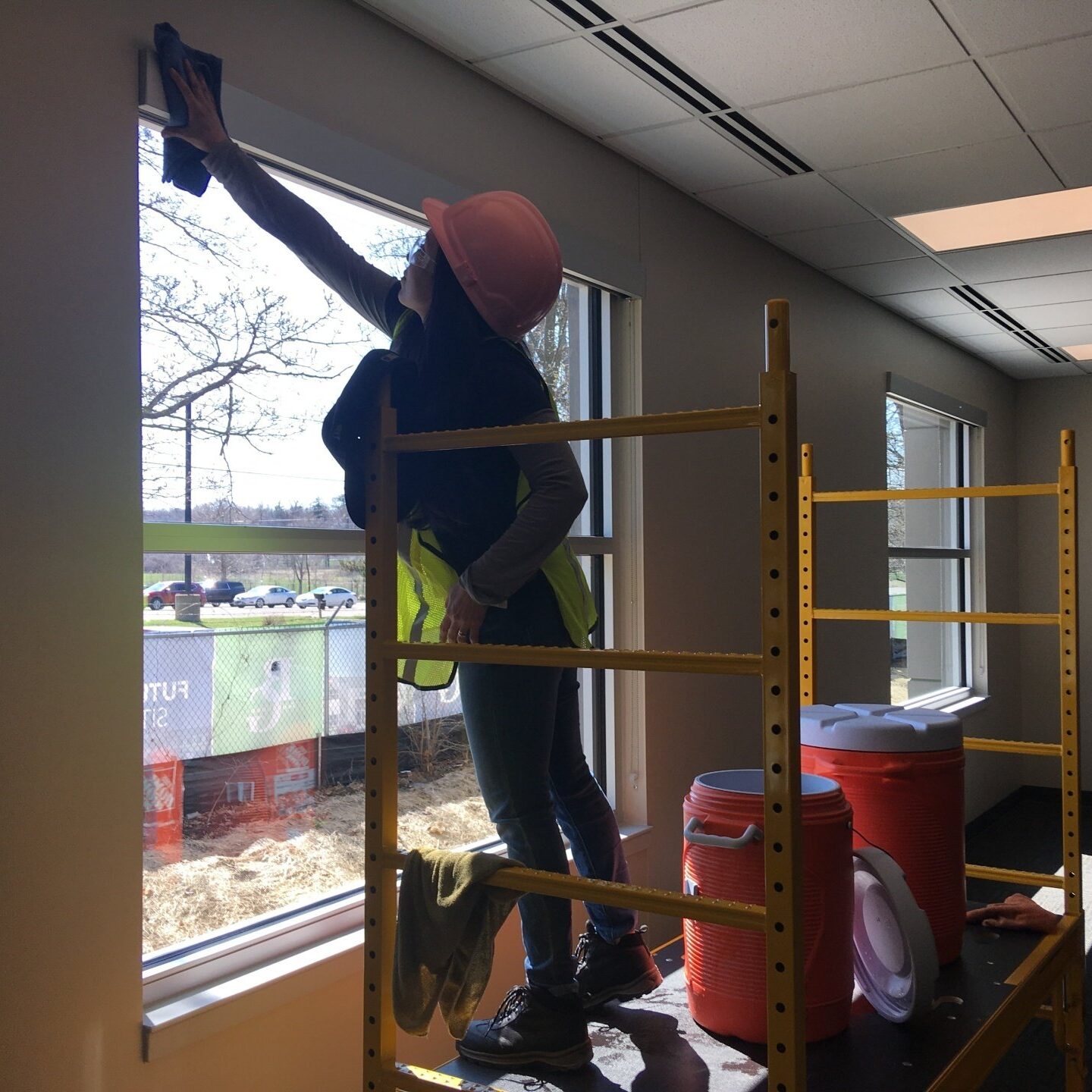 Construction worker in hard hat cleaning windows on scaffolding. Safety and cleaning services.